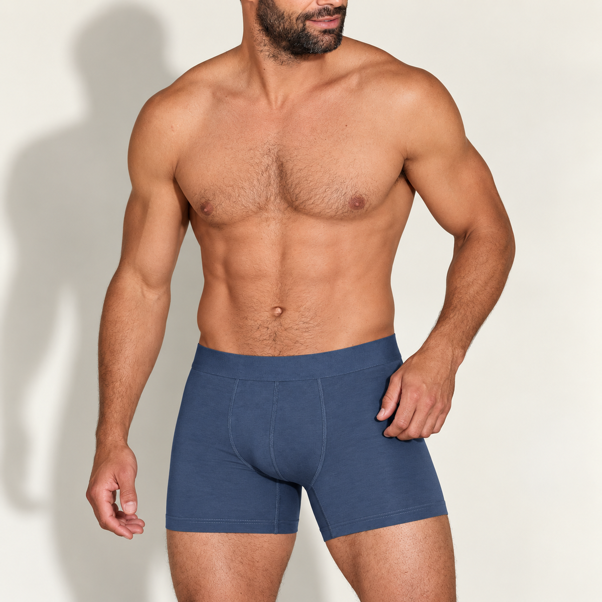 Muskulöser bärtiger Mann trägt blaue Boxerbriefs mit breitem Bund und Nähten am Eingriff, leicht seitlich gedreht.