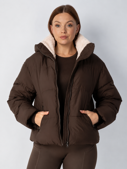 Model in brauner Steppjacke mit hellem Fleecefutter im Kragen, Hände in den Reißverschlusstaschen 14