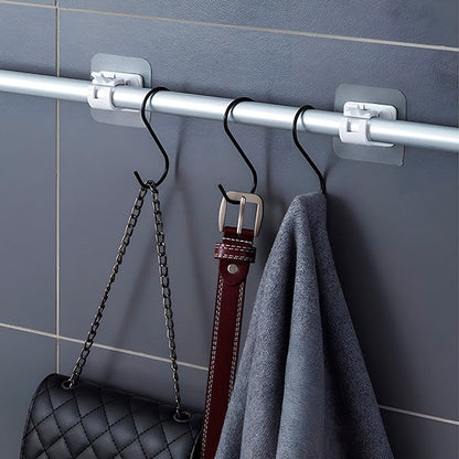 Detail einer Stange an zwei Halterungen an der Fliesenwand mit schwarzen S-Haken, Handtasche, braunem Gürtel und grauem Tuch.