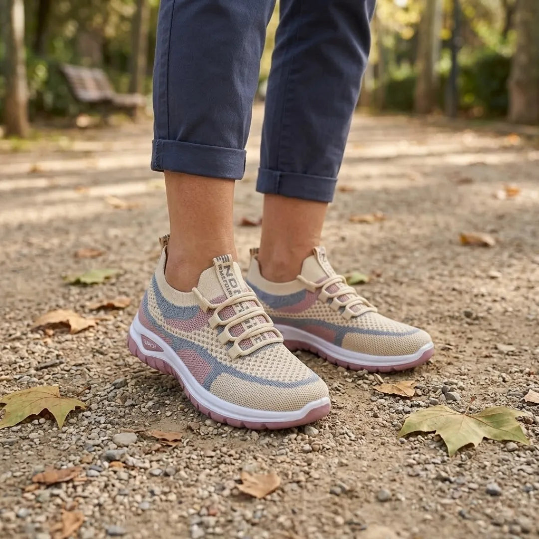 Frau trägt die beigen Sneaker mit rosa und blauen Akzenten beim Spaziergang auf einem Parkweg mit Herbstlaub 29