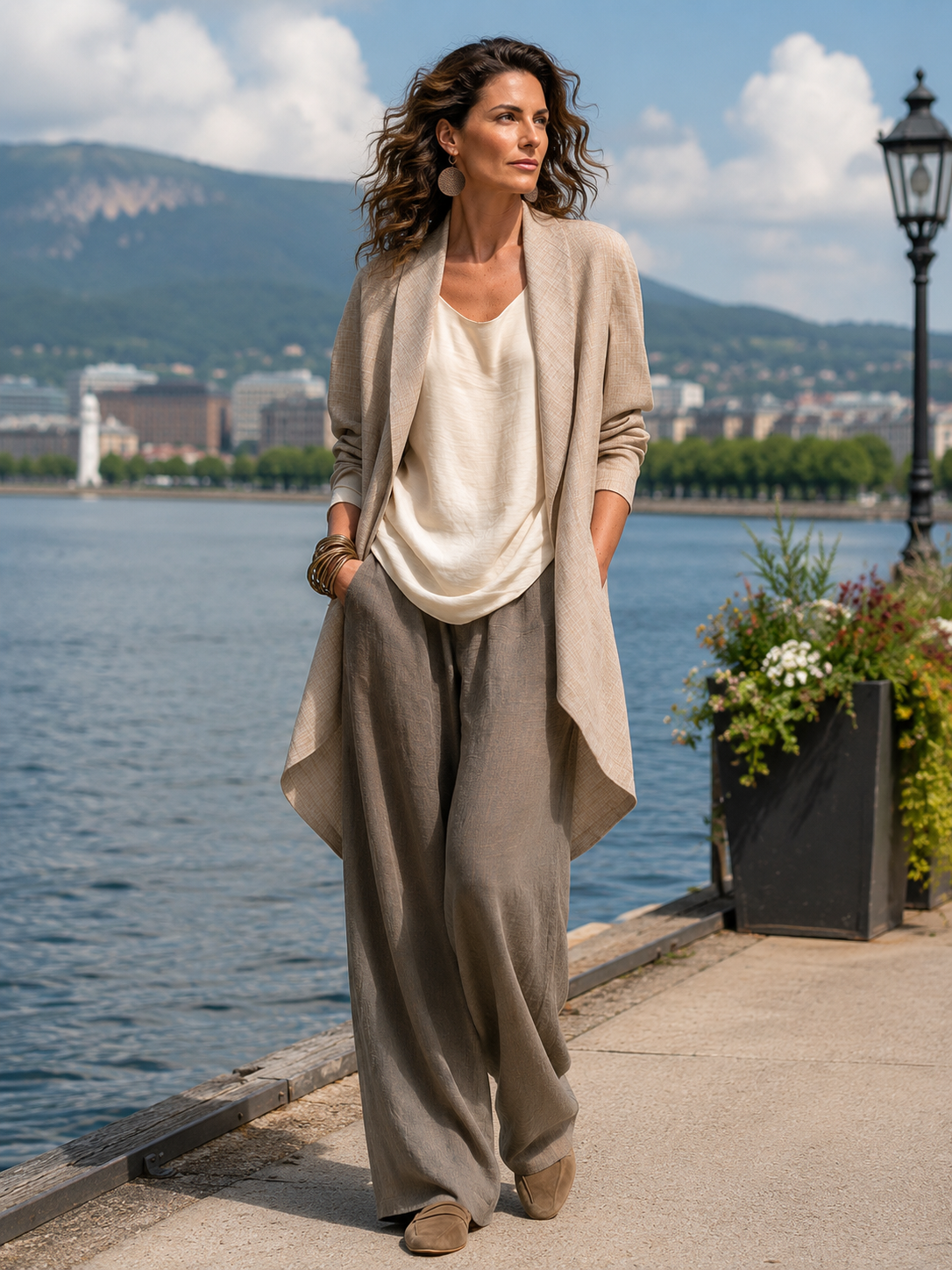 Frau trägt das dreiteilige Set im Freien an einer Seepromenade, Hände in den Hosentaschen, mit Blumenkübel und Laterne im Hintergrund. 7