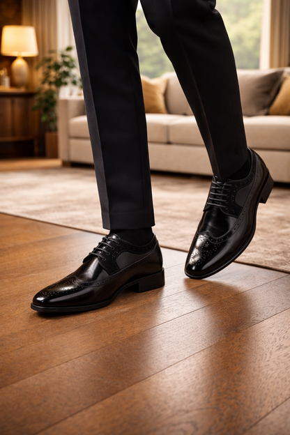 Schwarze, glänzende Brogue-Schnürschuhe mit Lochmuster, getragen im Gehen zu dunkler Anzughose vor einem Sofa. 2