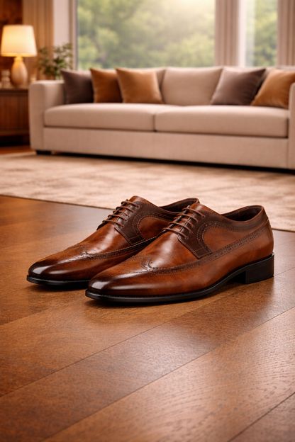 Paar brauner Leder-Brogues mit Lochverzierung und Schnürung, nebeneinander auf Holzboden vor einem beigen Sofa. 3