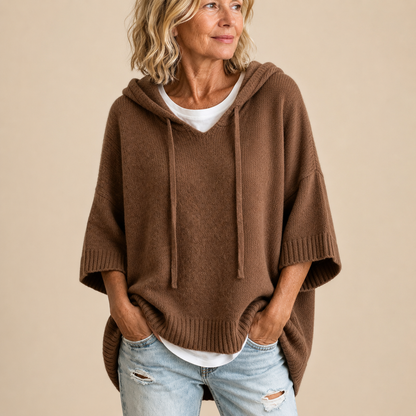 Brauner Strickponcho mit Kapuze, von einer lächelnden Frau in Halbfigur getragen.