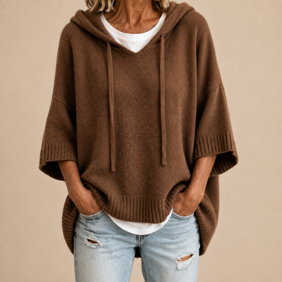 Brauner Strickponcho mit Kapuze und Dreiviertelärmeln, über weißem Shirt und hellen Jeans getragen, Nahaufnahme der Vorderseite. 3