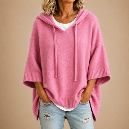 Rosafarbener Strickponcho mit Kapuze und weiten Dreiviertelärmeln, kombiniert mit weißem Shirt und hellblauen Jeans. 8