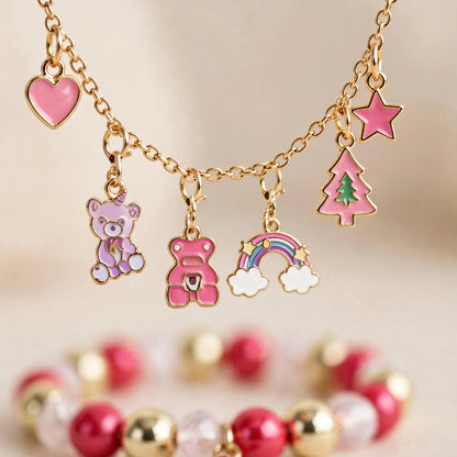 Nahaufnahme eines goldfarbenen Charm-Armbands mit rosa Anhängern wie Herz, Bär, Regenbogen, Tannenbaum und Stern, davor ein 3