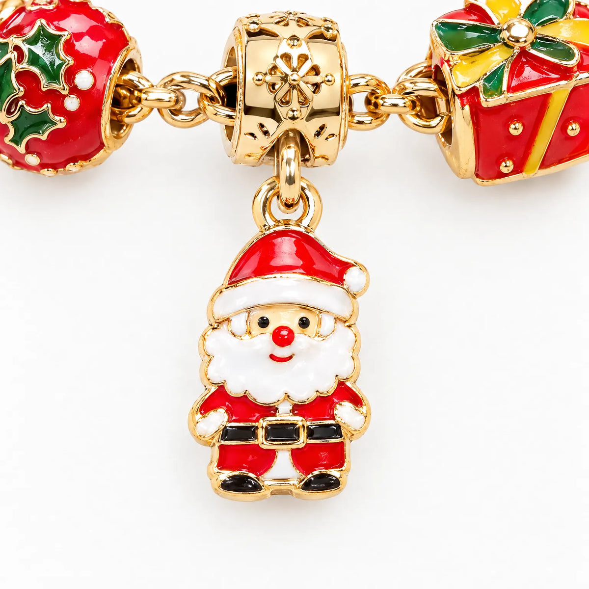 Nahaufnahme eines goldfarbenen Weihnachtsmann-Anhängers aus Emaille, daneben ein Stechpalmen-Charm und ein rotes Geschenk-Charm am Armband. 3