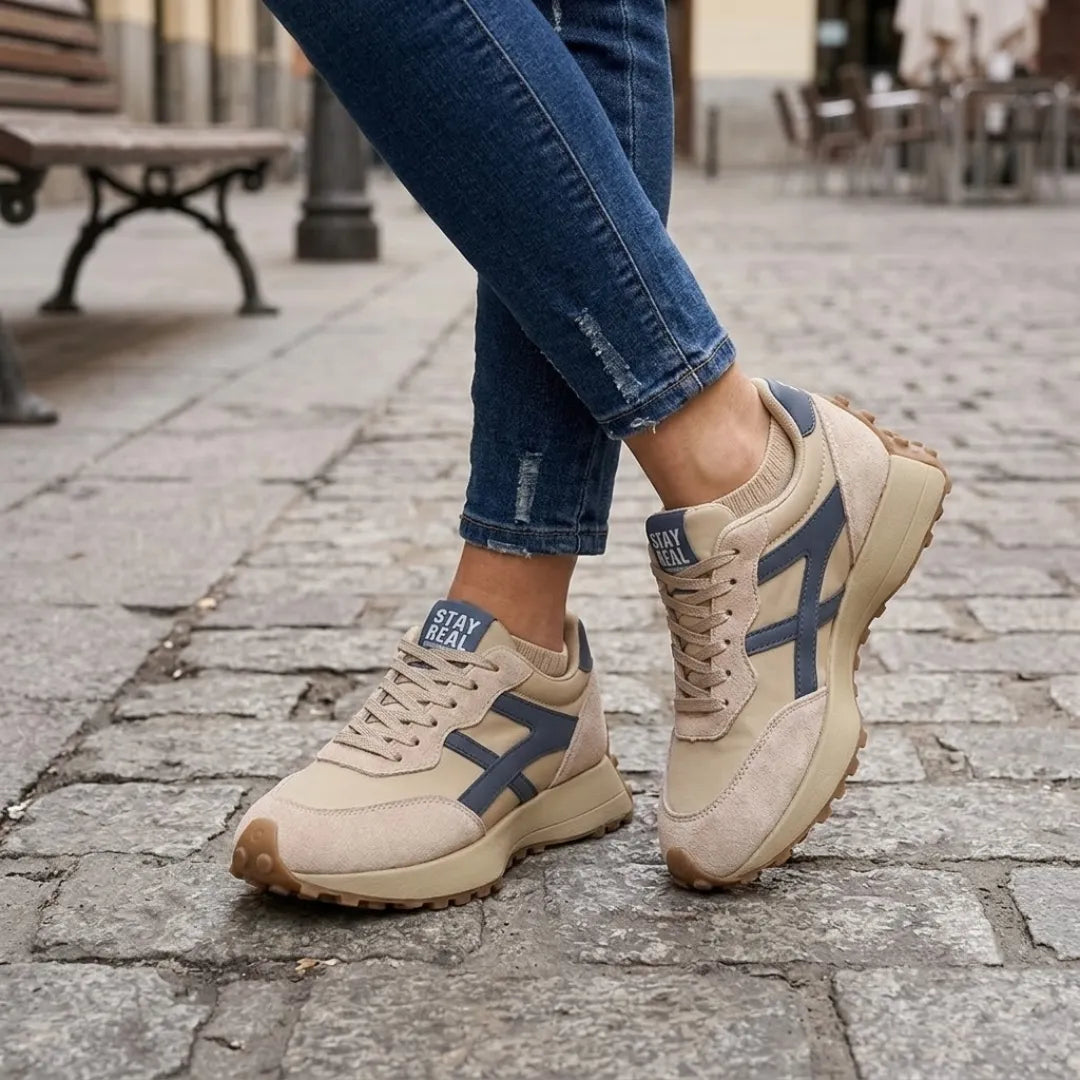 Beige Sneaker mit blauen Streifen, getragen zu zerrissener Jeans auf Kopfsteinpflaster 2