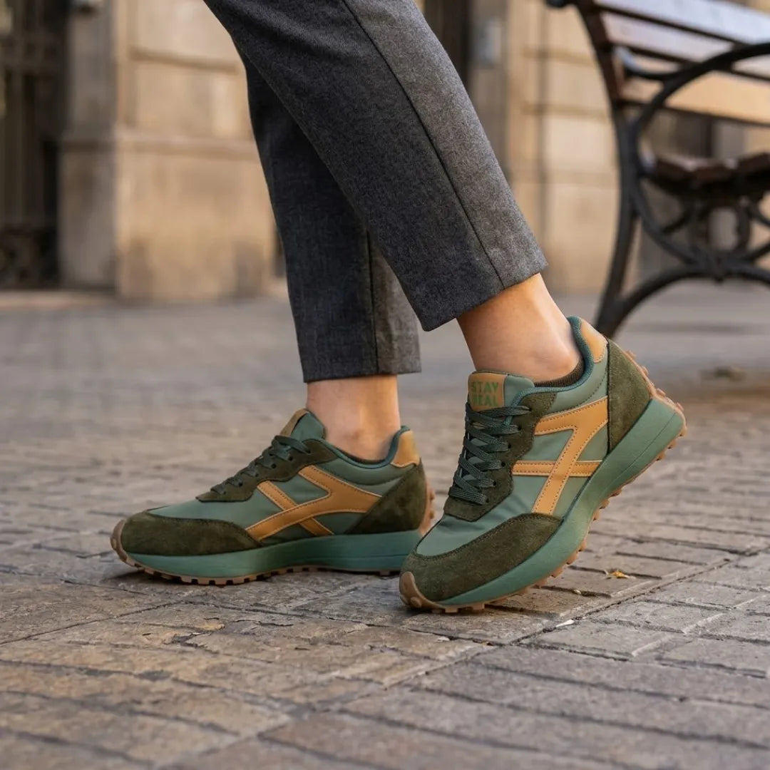 Grüne Sneaker mit orangebraunen Streifen, getragen zu grauer Hose auf Kopfsteinpflaster 12