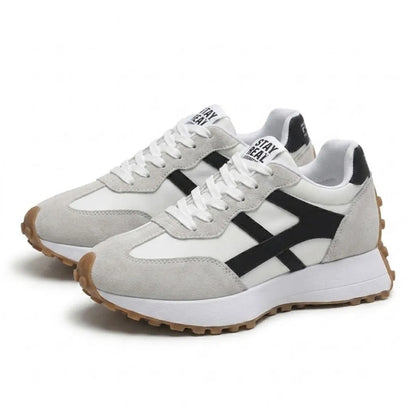 Sneaker-Paar von schräg vorn, weiße Schnürsenkel, helles Wildleder, schwarze Seitenstreifen und honigfarbene Noppensohle 23
