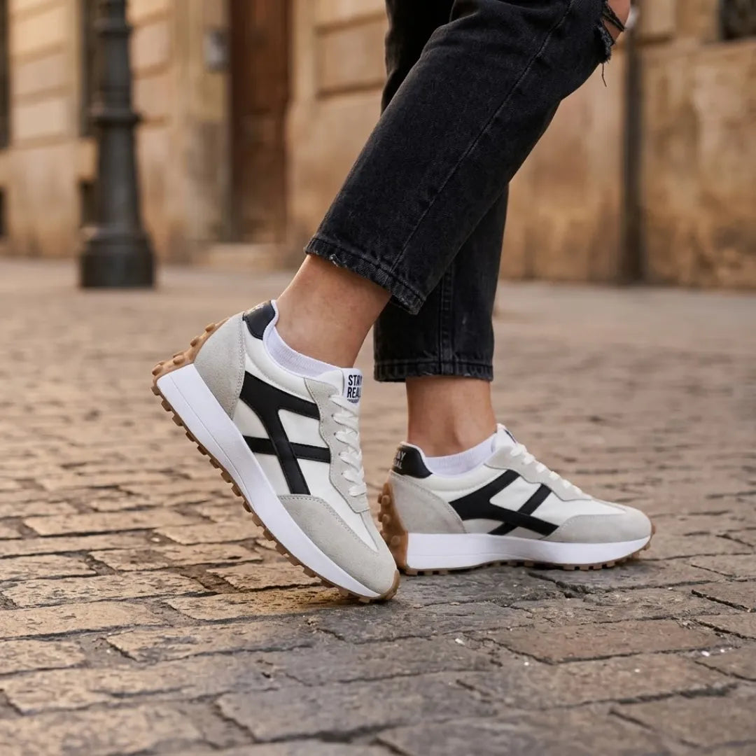 Sneaker an den Füßen einer Frau in schwarzer Jeans auf Kopfsteinpflaster 22