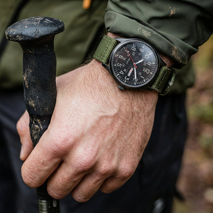 Herrenuhr im Feldstil mit grünem Stoffarmband als Detail am Handgelenk.