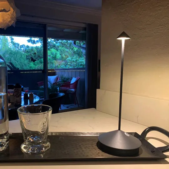 Dunkle Lampe auf einem Tablett neben einem Glas, dahinter eine Terrasse mit Sitzgelegenheiten 19