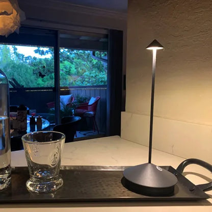 Dunkle Lampe auf einem Tablett neben einem Glas, dahinter eine Terrasse mit Sitzgelegenheiten 19