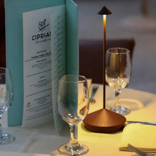 Braune, leuchtende Tischlampe auf einem gedeckten Restaurant-Tisch neben Weingläsern und einer aufgestellten Speisekarte 21