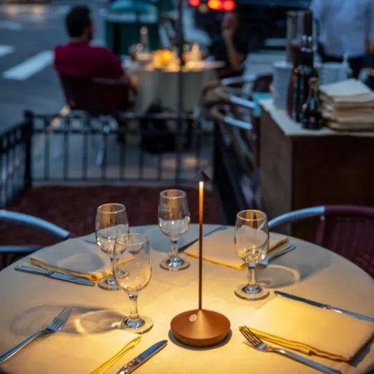 Leuchtende Lampe auf einem gedeckten Restauranttisch im Freien mit Gläsern, Besteck und Servietten 4