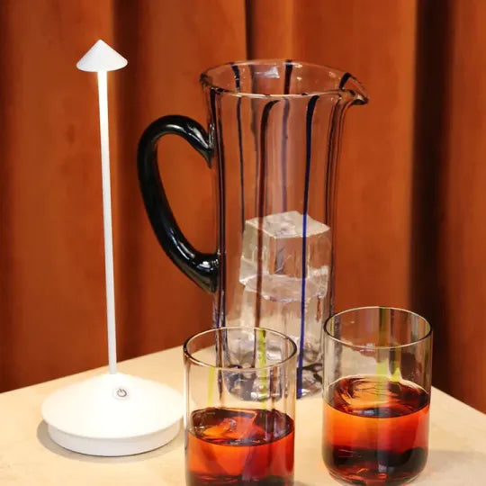 Weiße Lampe neben einer Glaskaraffe mit Eiswürfeln und zwei Gläsern vor orangefarbenem Vorhang 6
