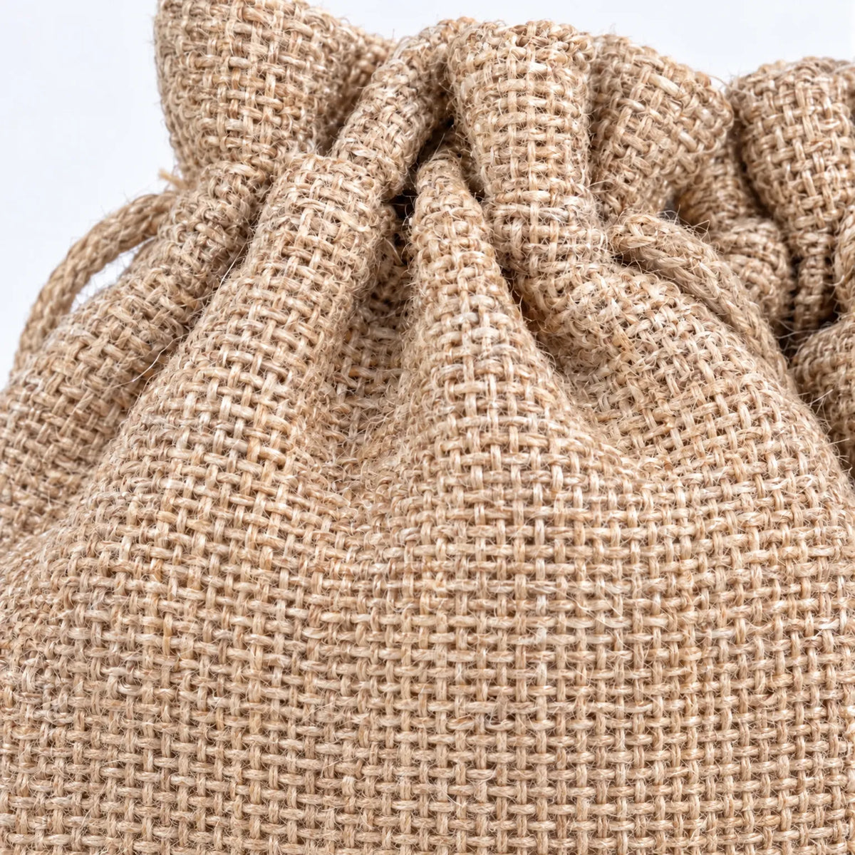 Nahaufnahme eines Beutels mit Kordelzug, die das grobe, natürliche Gewebe aus Jute und die gerafften Falten am oberen Rand zeigt. 3