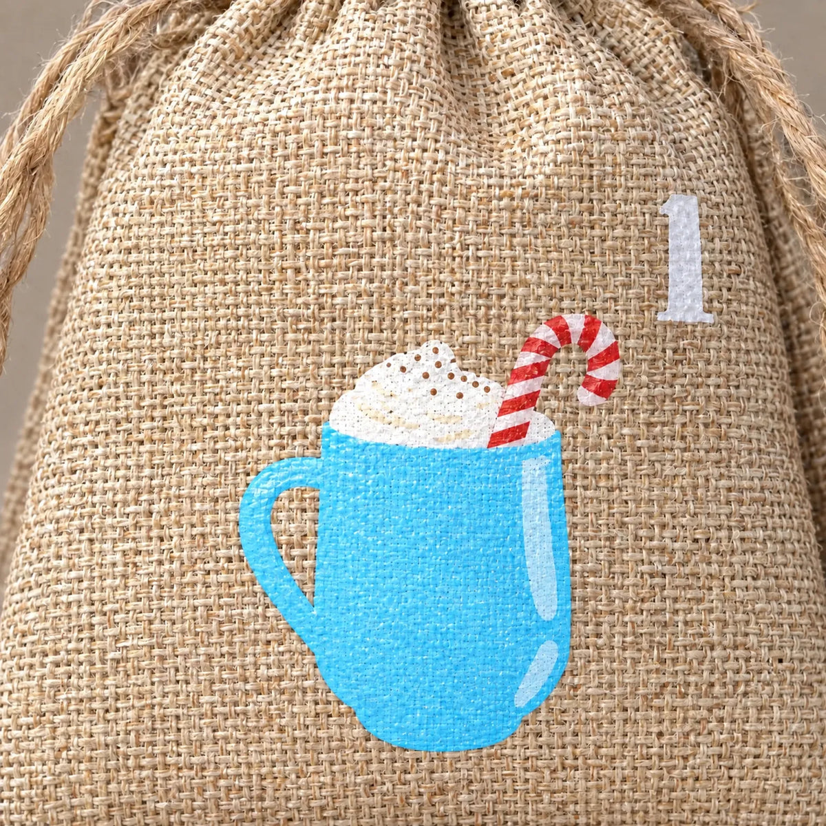 Nahaufnahme eines Jutebeutels mit grob gewebtem Stoff, Zugband und aufgedruckter blauer Tasse mit Sahne und Zuckerstange neben der Zahl. 3