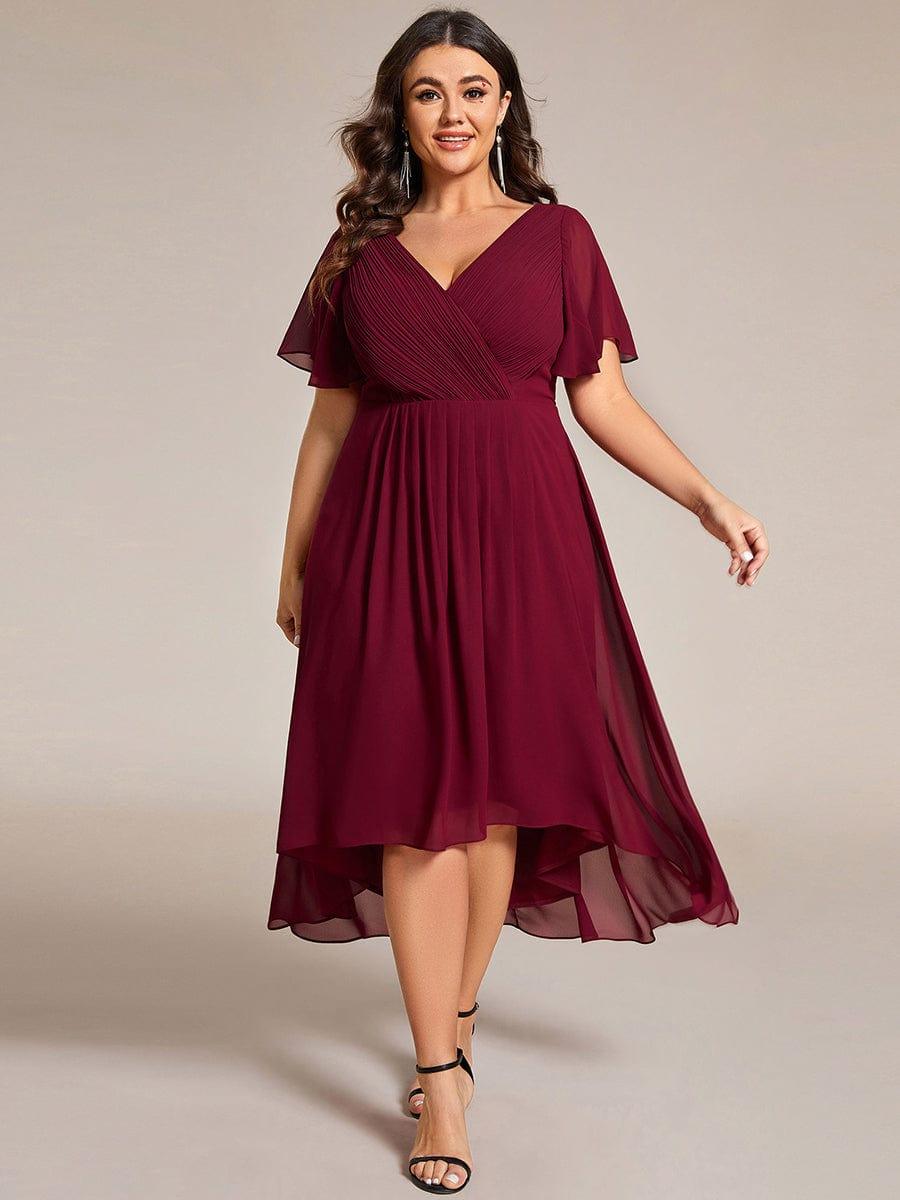 Plus-Size-Model im weinroten Hoch-Tief-Kleid mit Flatterärmeln und schwarzen Sandalen, lange Ohrringe, leichte Gehbewegung. 49