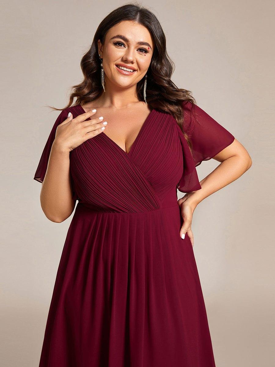 Nahaufnahme des weinroten Oberteils an einer Plus-Size-Trägerin, Raffung am Wickelausschnitt und transparente Flatterärmel. 51