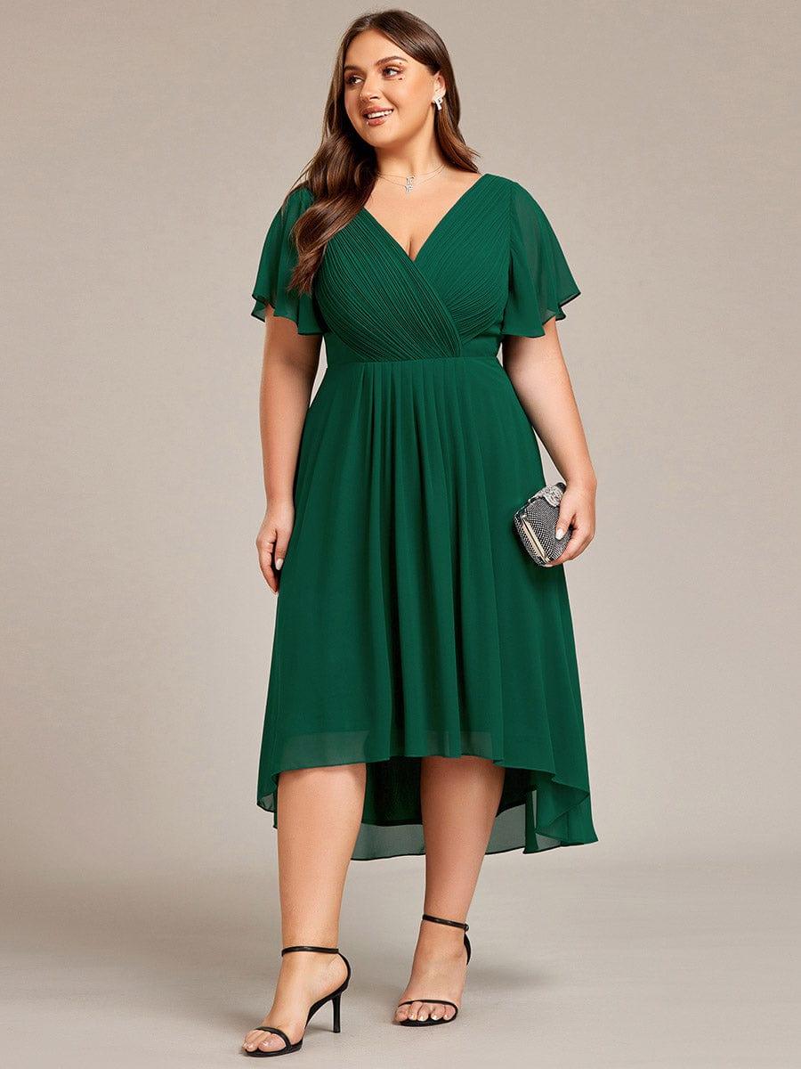 Frontansicht des dunkelgrünen Chiffonkleids an einem Curvy Model mit kleiner Clutch, plissiertem Wickeloberteil und schwarzen Absatzsandaletten. 40