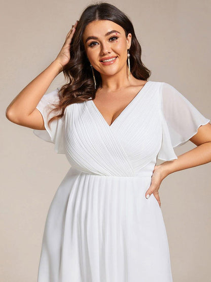 Nahaufnahme des weißen, gerafften V-Ausschnitts mit Flatterärmeln an einem lächelnden Plus-Size-Model mit Fransenohrringen. 75