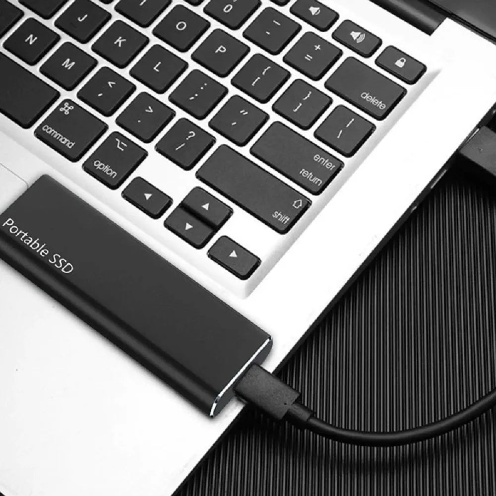 Schwarze externe Festplatte per USB-C-Kabel neben der Tastatur eines Laptops.