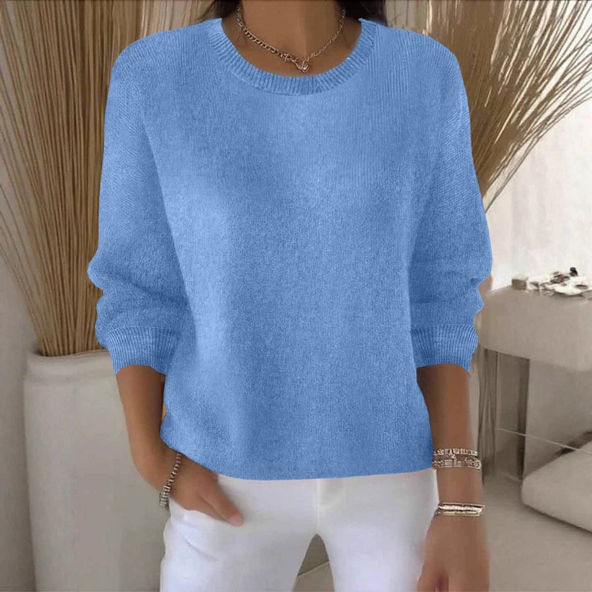 Frau im hellblauen Strickpullover mit Rundhals, kombiniert mit weißer Hose und Armbändern 13