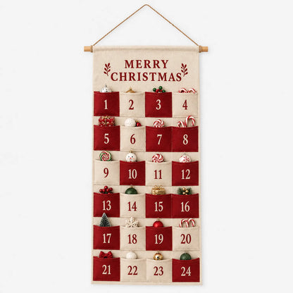 Frontansicht des Stoffkalenders mit Holzstab und Hängeschnur vor weißem Hintergrund, die 24 Taschen sind mit kleinen Weihnachtsdekorationen gefüllt. 2
