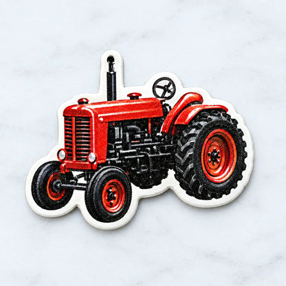 Nahaufnahme eines einzelnen Anhängers in Form eines roten Oldtimer-Traktors mit weißem Rand und kleinem Aufhängeloch, auf hellem Marmorhintergrund. 3