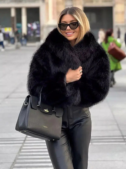 Lächelnde Frau in schwarzem Kunstpelzmantel mit Sonnenbrille, schwarzer Handtasche und Lederhose auf einem Platz 7