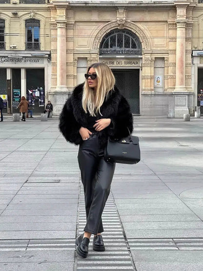 Ganzkörperbild einer Frau im schwarzen Kunstpelzmantel mit Lederhose, Plateauschuhen und schwarzer Tasche 8