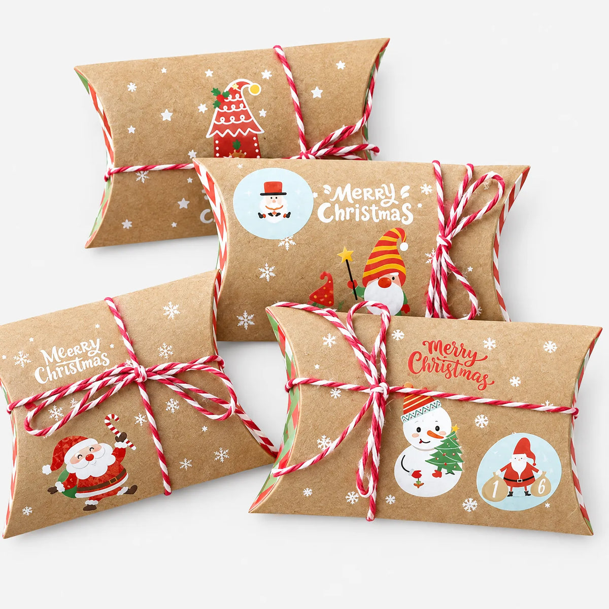 Vier Kissenboxen aus Kraftpapier mit rot-weißer Kordel und unterschiedlichen Weihnachtsmotiven wie Schneemann, Wichtel und Weihnachtsmann auf hellem Hintergrund 2