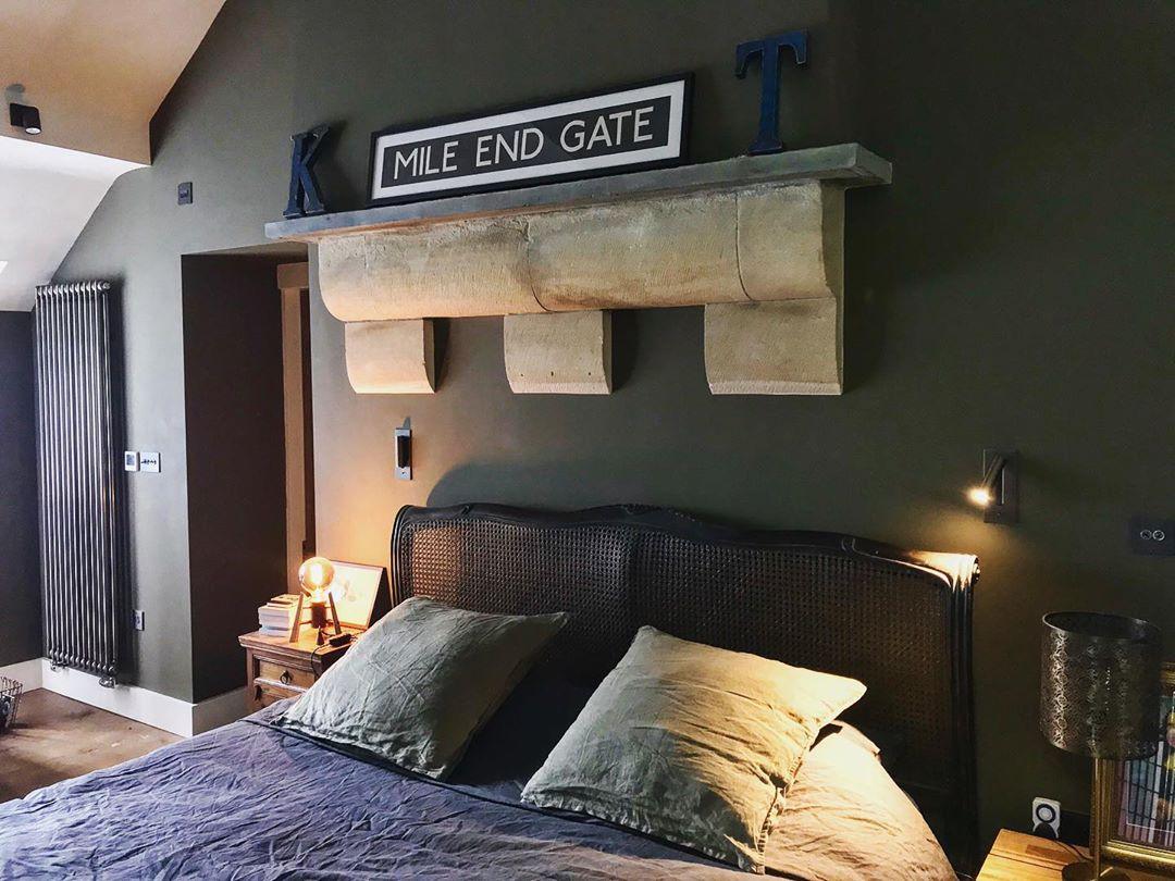 Schlafzimmer mit dunkelgrüner Wand und Bett, zwei schwarze Wandleuchten, eine davon leuchtend, am Kopfende 37