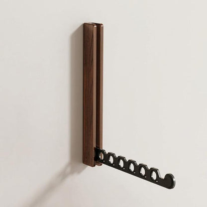 Ausgeklappter Wandhaken aus dunklem Holz mit schwarzem Arm und sechs runden Löchern, einzeln vor heller Wand. 6