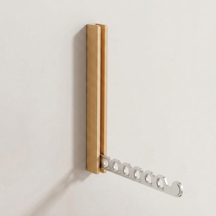 Wandhaken aus hellem Holz mit ausgeklapptem silbernem Metallarm und sechs runden Löchern vor heller Wand. 9
