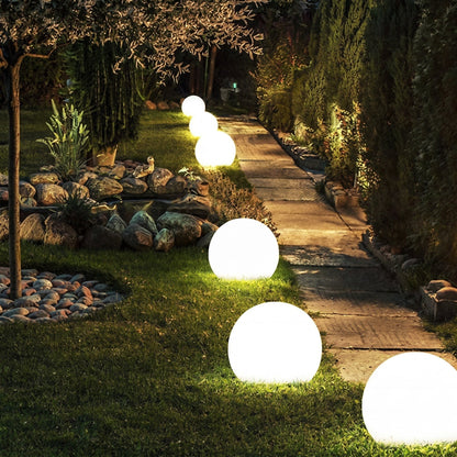 Reihe leuchtender Kugelleuchten entlang eines gepflasterten Gartenwegs auf dem Rasen. 6
