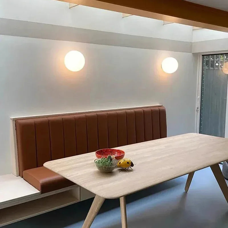 Zwei Kugelleuchten an einer weißen Wand über einer braunen Sitzbank und einem Holztisch 12