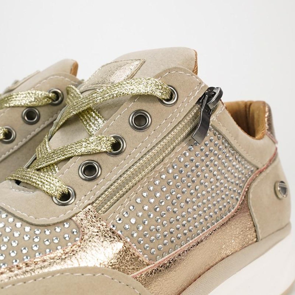 Nahaufnahme von Schnürung, Metallösen, Seitenreißverschluss und Strasssteinen am beigen Schuh mit goldenen Schnürsenkeln.