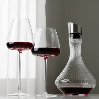 Zwei Gläser mit Rotwein neben einer gerippten Glaskaraffe mit Metallverschluss vor einem hellen Vorhang 3