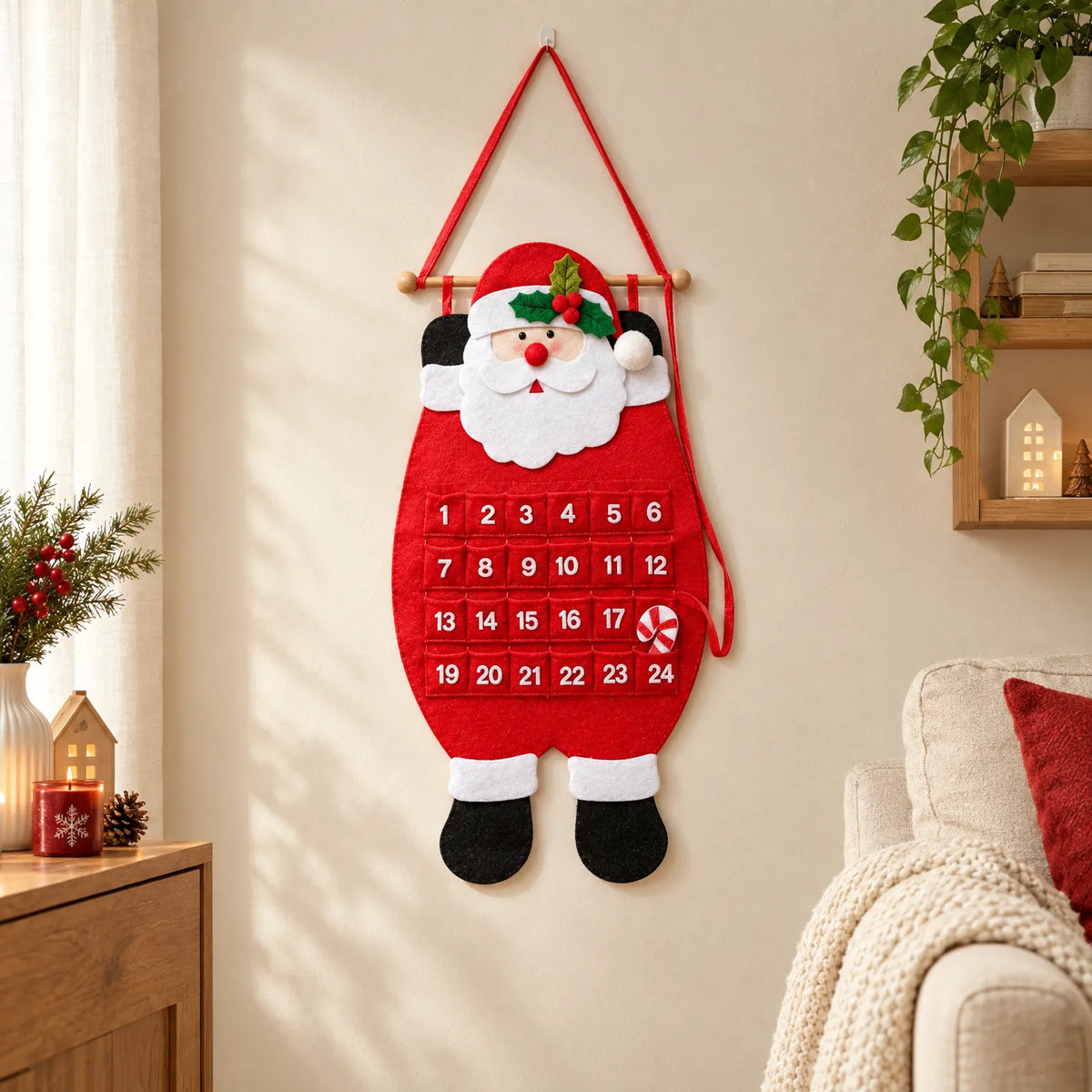 Roter Filz-Adventskalender in Weihnachtsmannform hängt an einer hellen Wand in einem weihnachtlich dekorierten Wohnzimmer neben Regal, Kerze und Sofa. 1