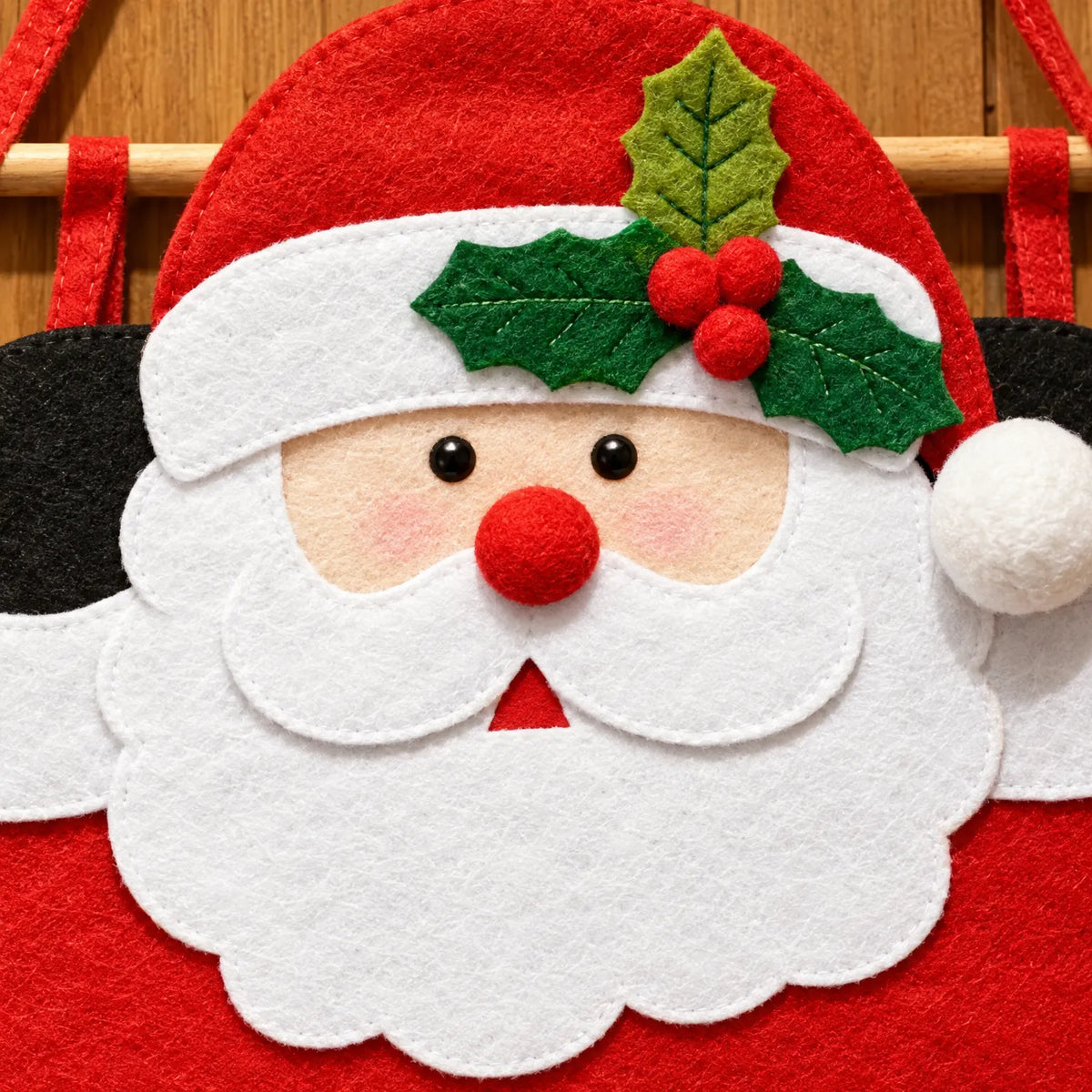 Nahaufnahme des Weihnachtsmanngesichts aus Filz mit Stechpalmenzweig, roter Pompon-Nase, weißem Bart und aufgenähten Details. 3