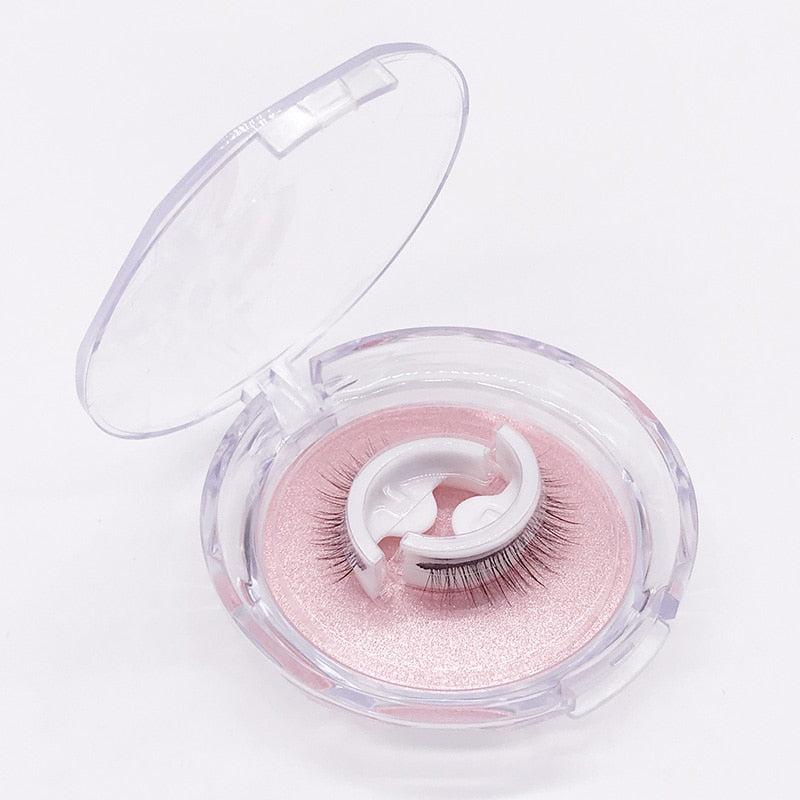 Geöffnete runde Klarsichtbox auf weißem Hintergrund, darin ein Wimpernpaar auf weißem Halter über rosa glitzerndem Einleger. 6