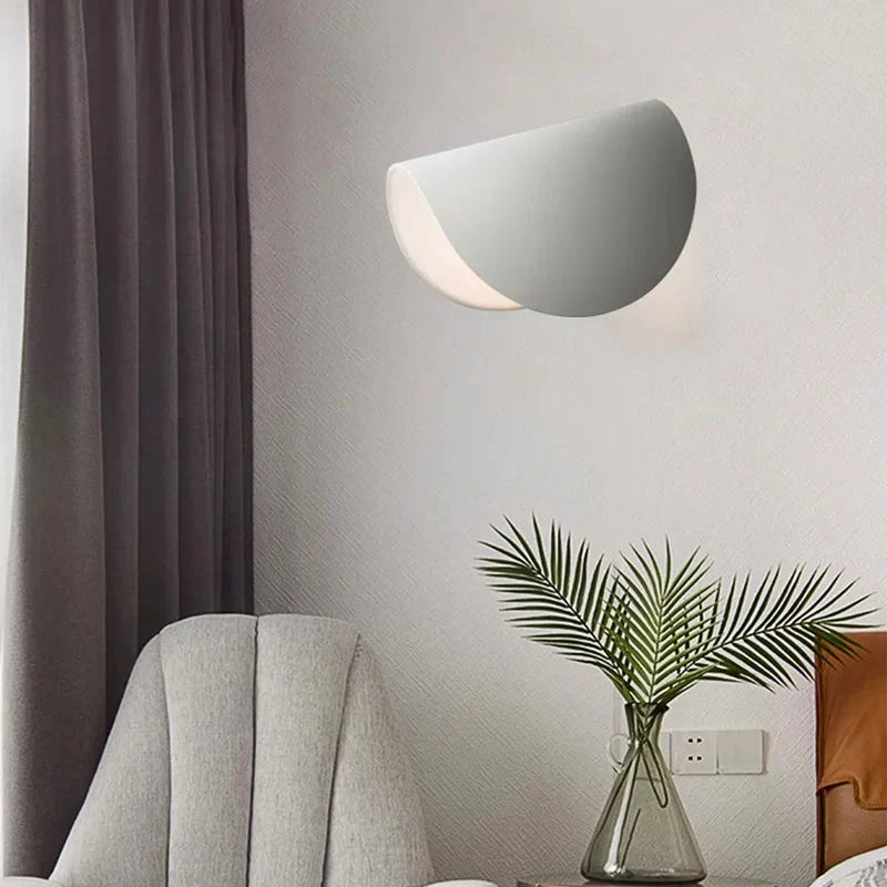 Weiße, schalenförmig geöffnete Wandleuchte über einem grauen Sessel im Wohnraum.