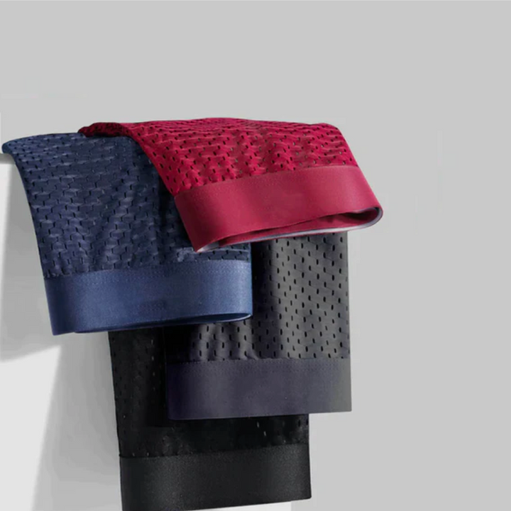 Drei Boxershorts in Rot, Blau und Schwarz hängen mit sichtbarem Lochmuster über einer Kante 3