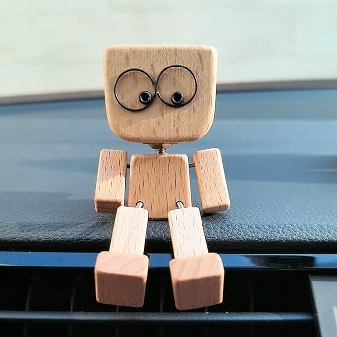 Holzfigur mit großen runden Augen auf der Kante eines Armaturenbretts über einem Lüftungsgitter.