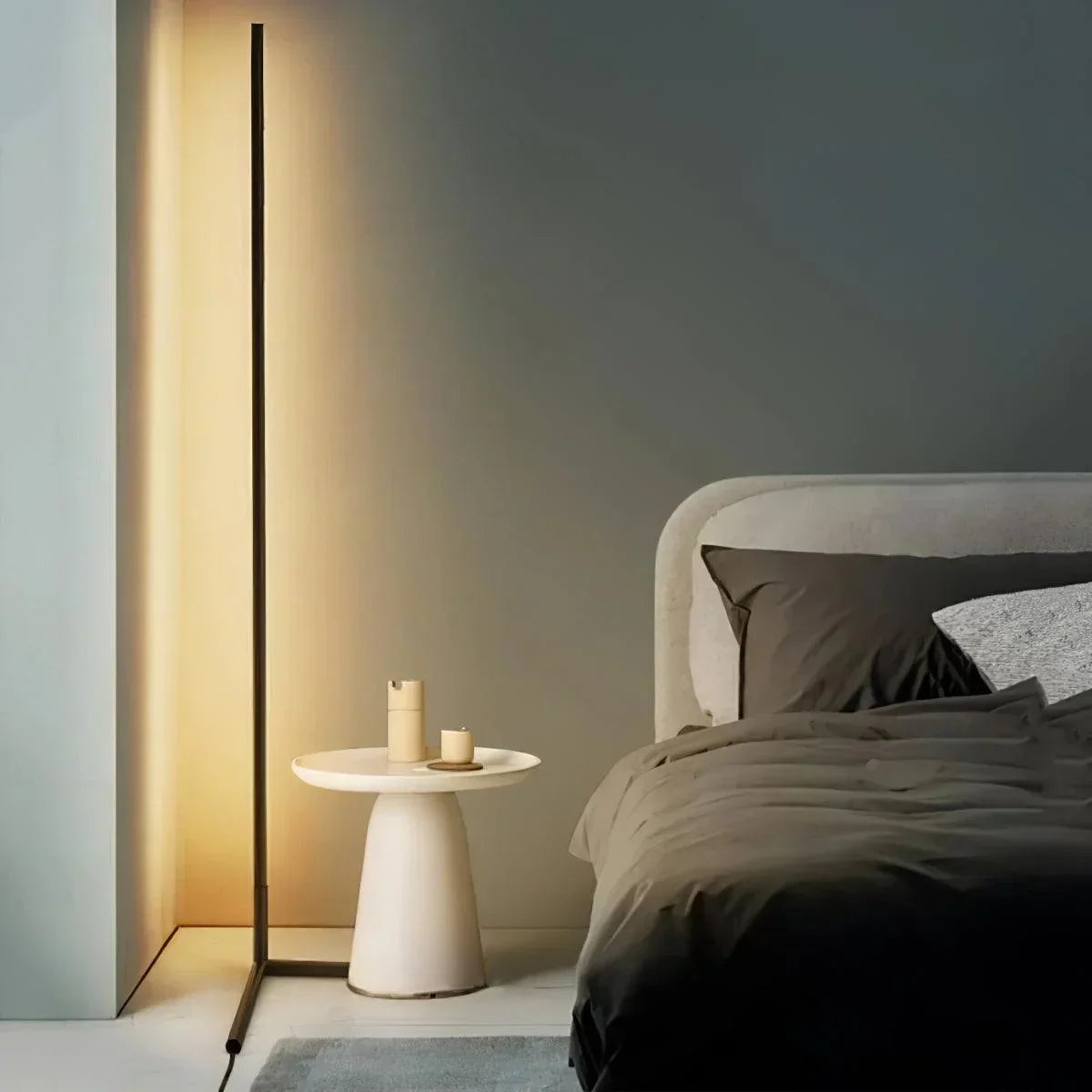 Leuchtende schwarze Stehlampe neben einem hellen Beistelltisch und einem Bett mit dunkler Bettwäsche 1