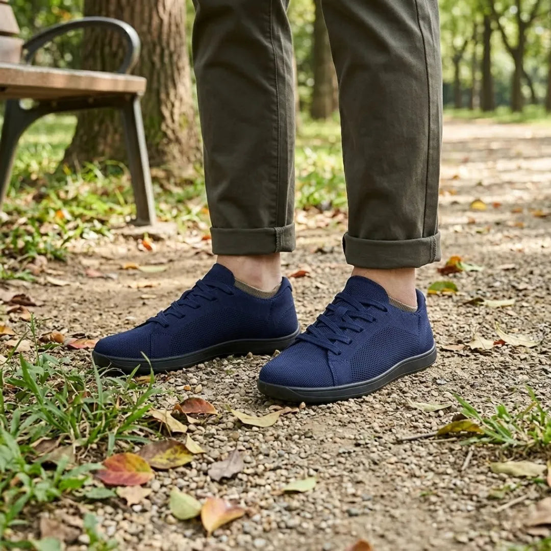 Marineblaue Sneaker mit schwarzer Sohle an den Füßen einer Person in olivgrüner Hose, im Park neben einer Bank. 20
